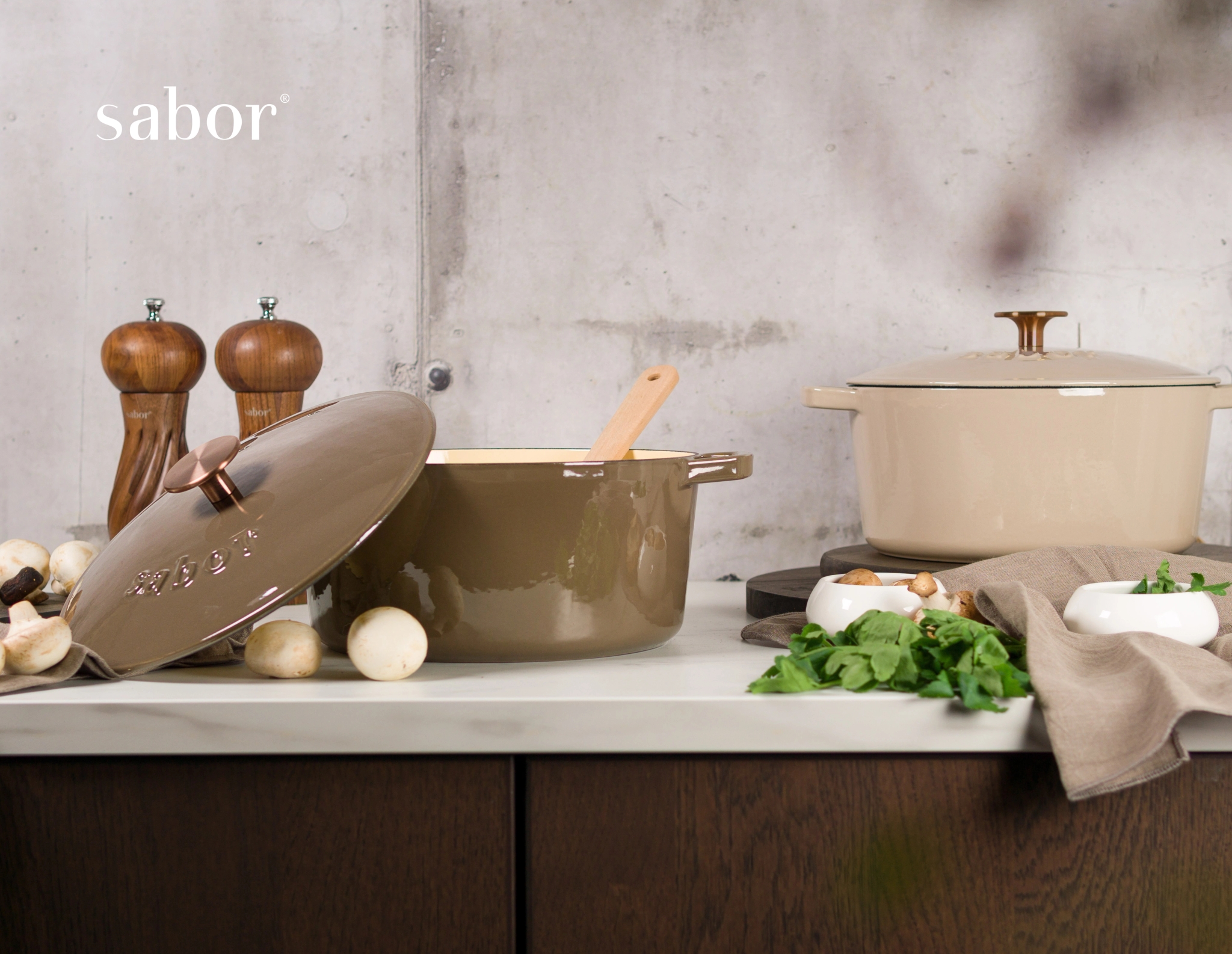 Sabor gjutjärnsgrytor i brunt och beige med svamp, örter och kvarnar på en köksbänk.