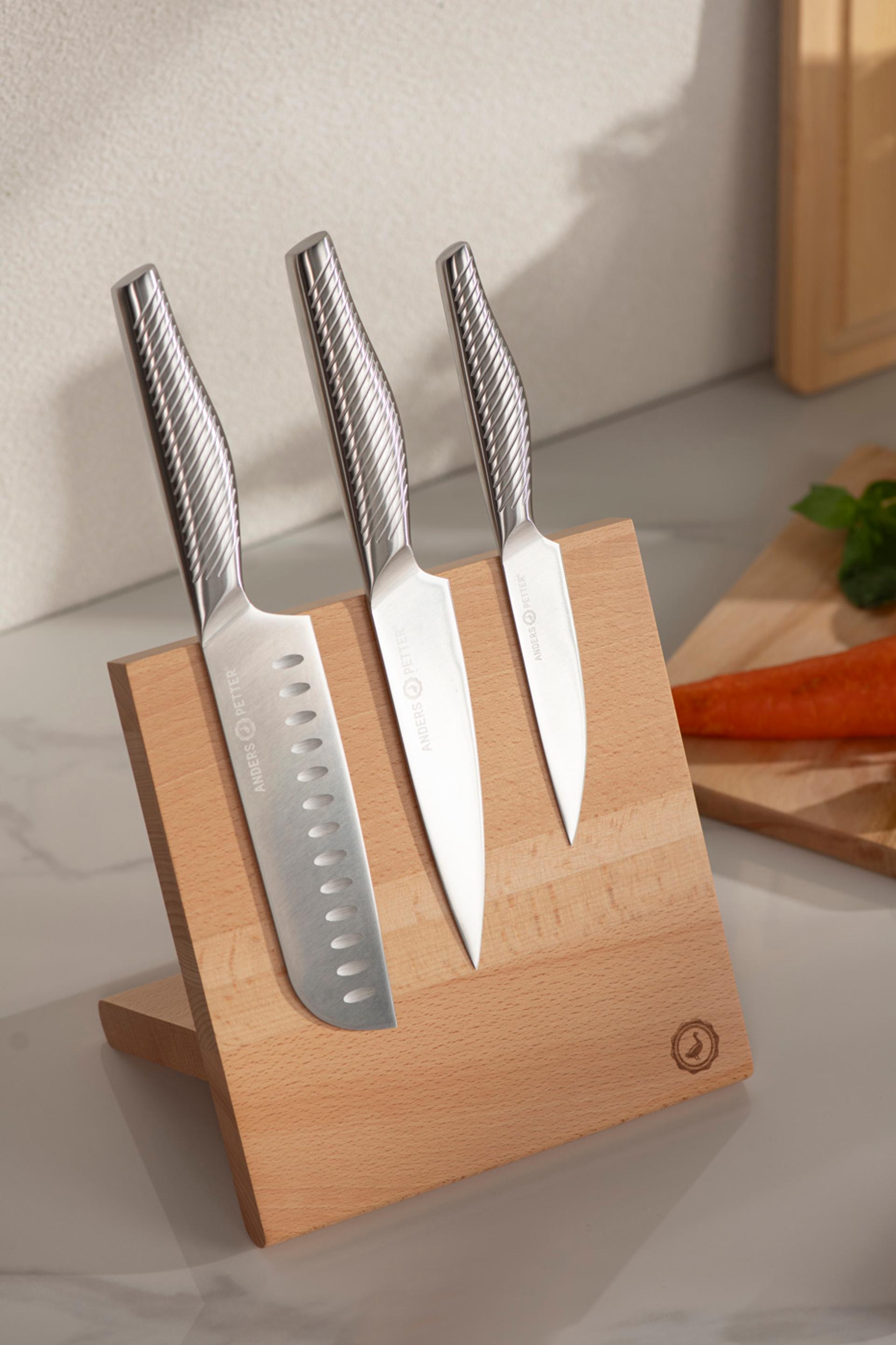 Tre stilrena köksknivar i rostfritt stål står i ett magnetiskt knivblock av trä på en köksbänk.