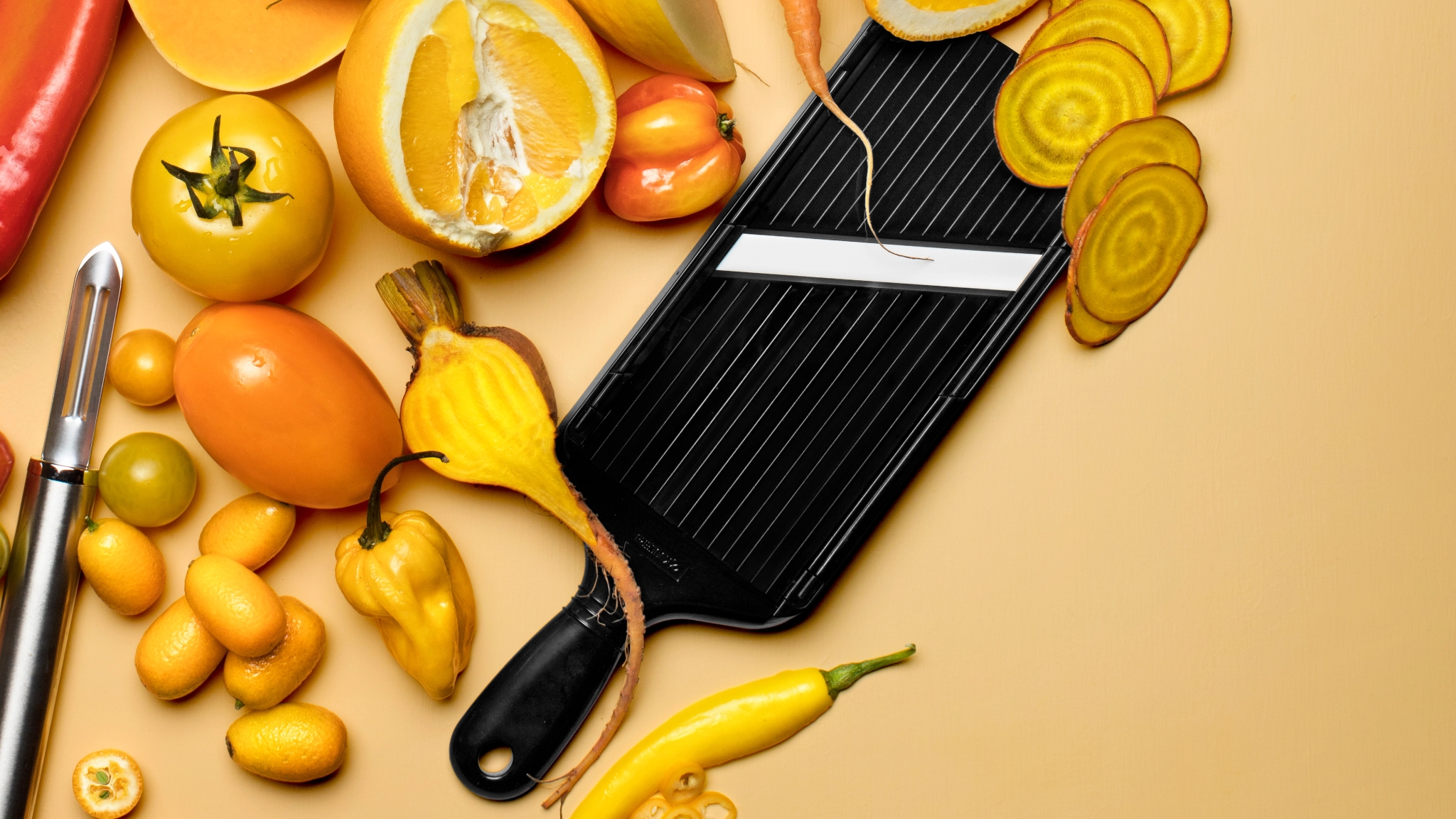 Kyocera keramisk mandolin med rotfrukter, sitrusfrukter og tomater i gule og oransje toner.