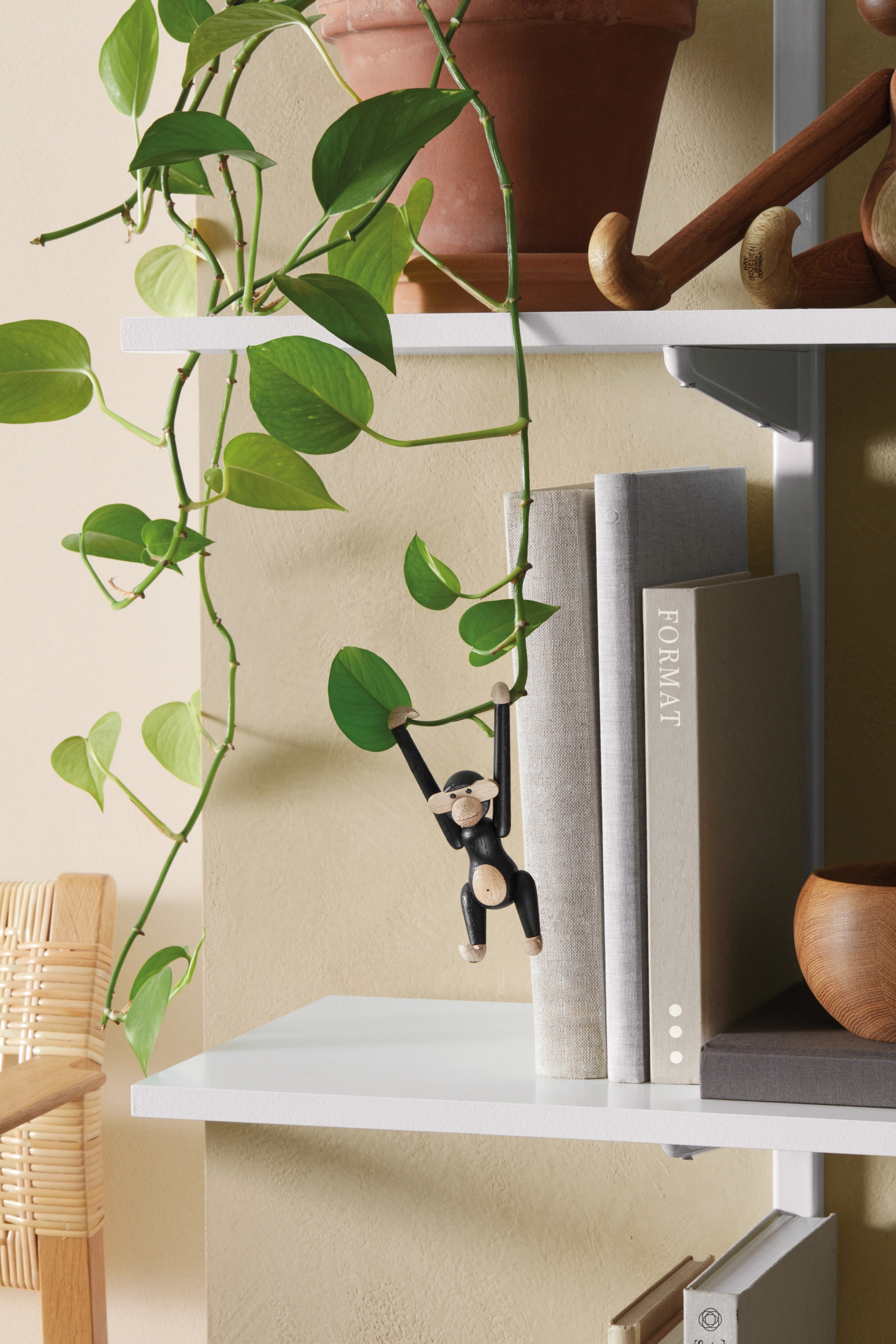 två vita hyllplan med böcker och krukor på sig med en Kay Bojesen apa i svart hängandes 