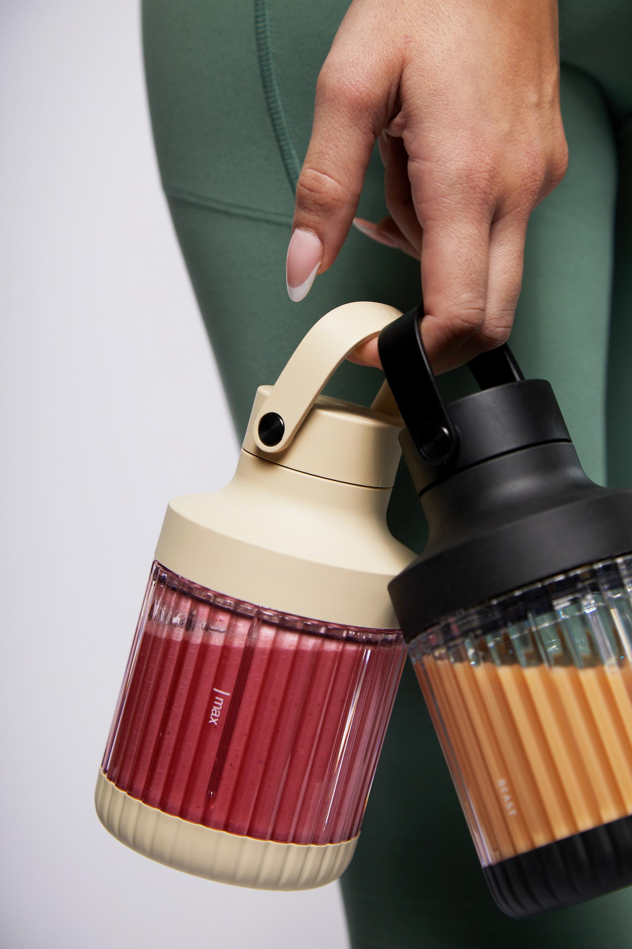 En person håller i två to go muggar med smoothies 
