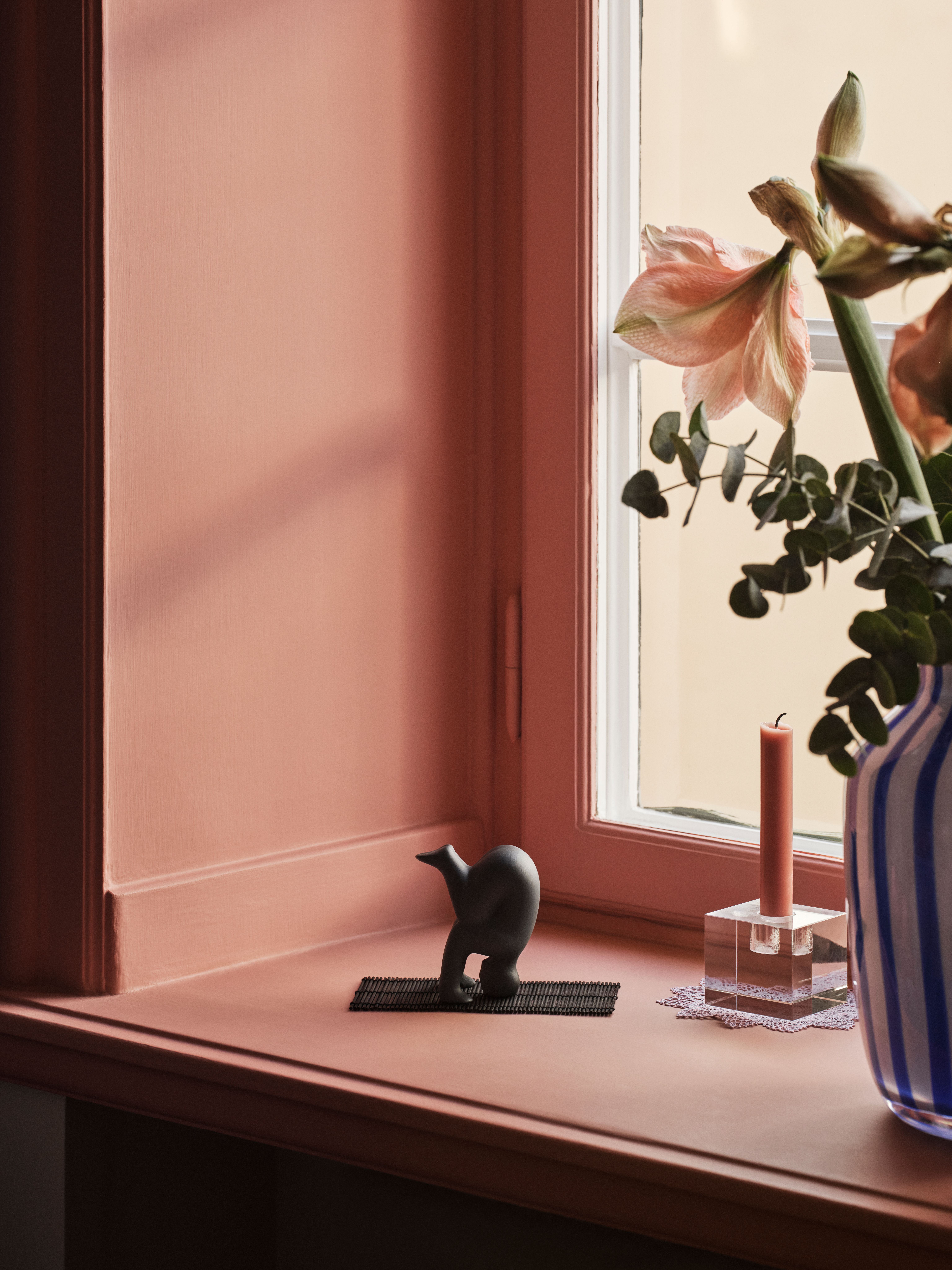 Lisa Larson Yoga figur i svart på en fönsterbräda mot en rosa vägg