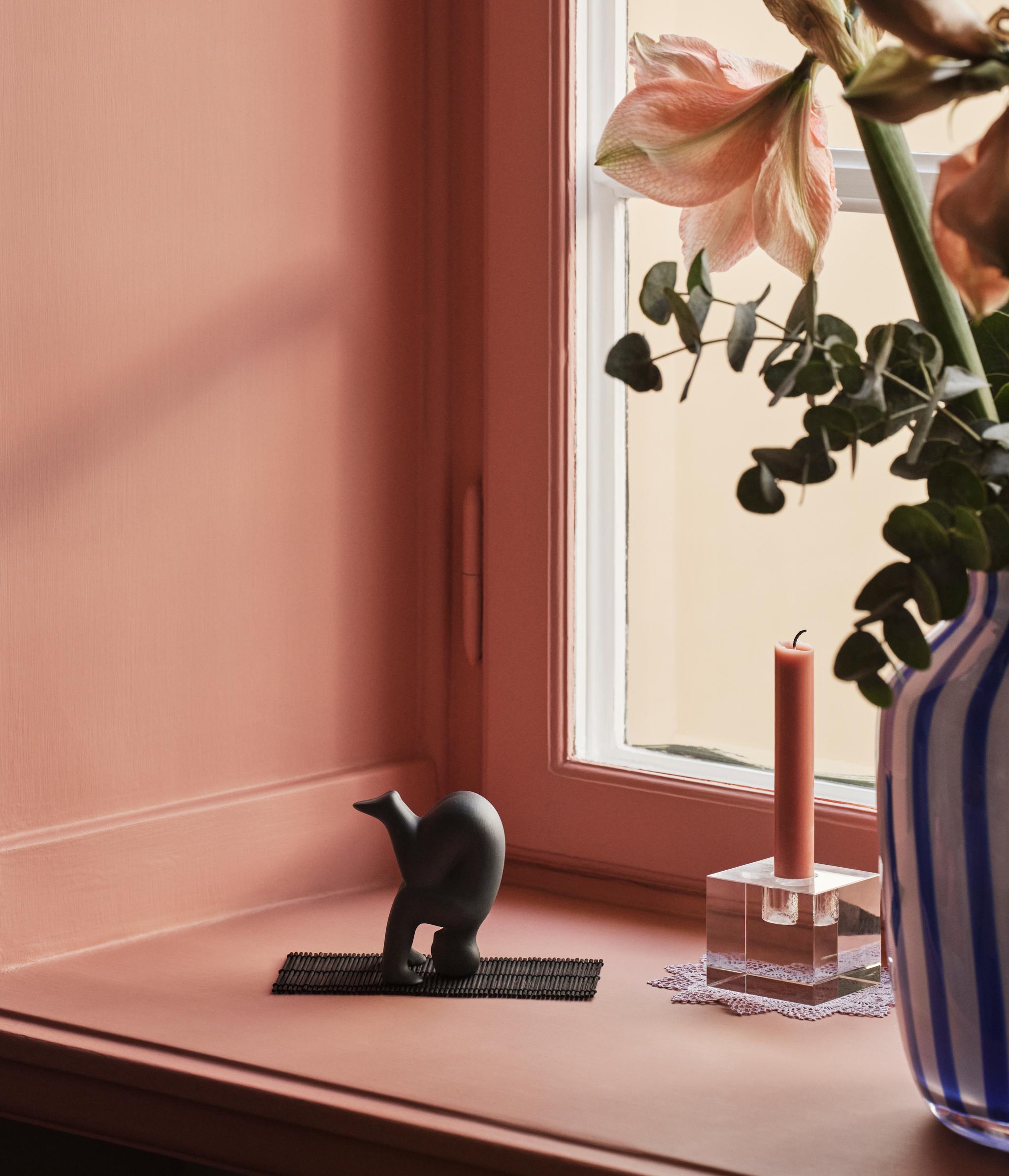 Lisa Larson Yoga figur i svart på en fönsterbräda mot en rosa vägg