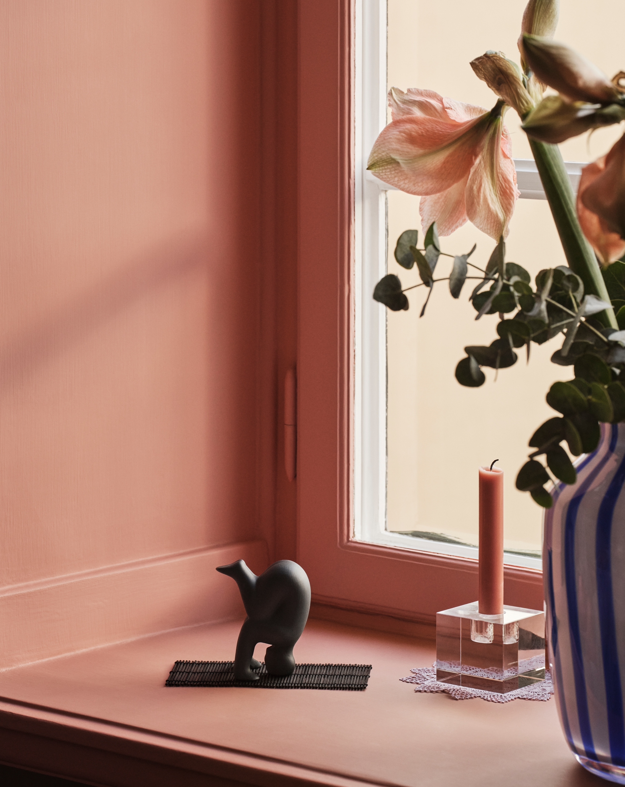 Lisa Larson Yoga figur i svart på en fönsterbräda mot en rosa vägg