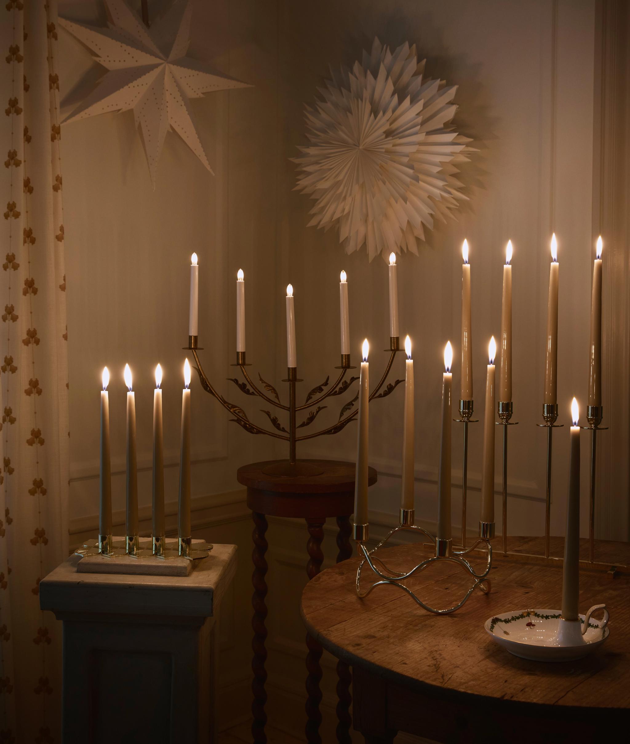 Julstjärnor och tända adventsljusstakar mot en vit vägg