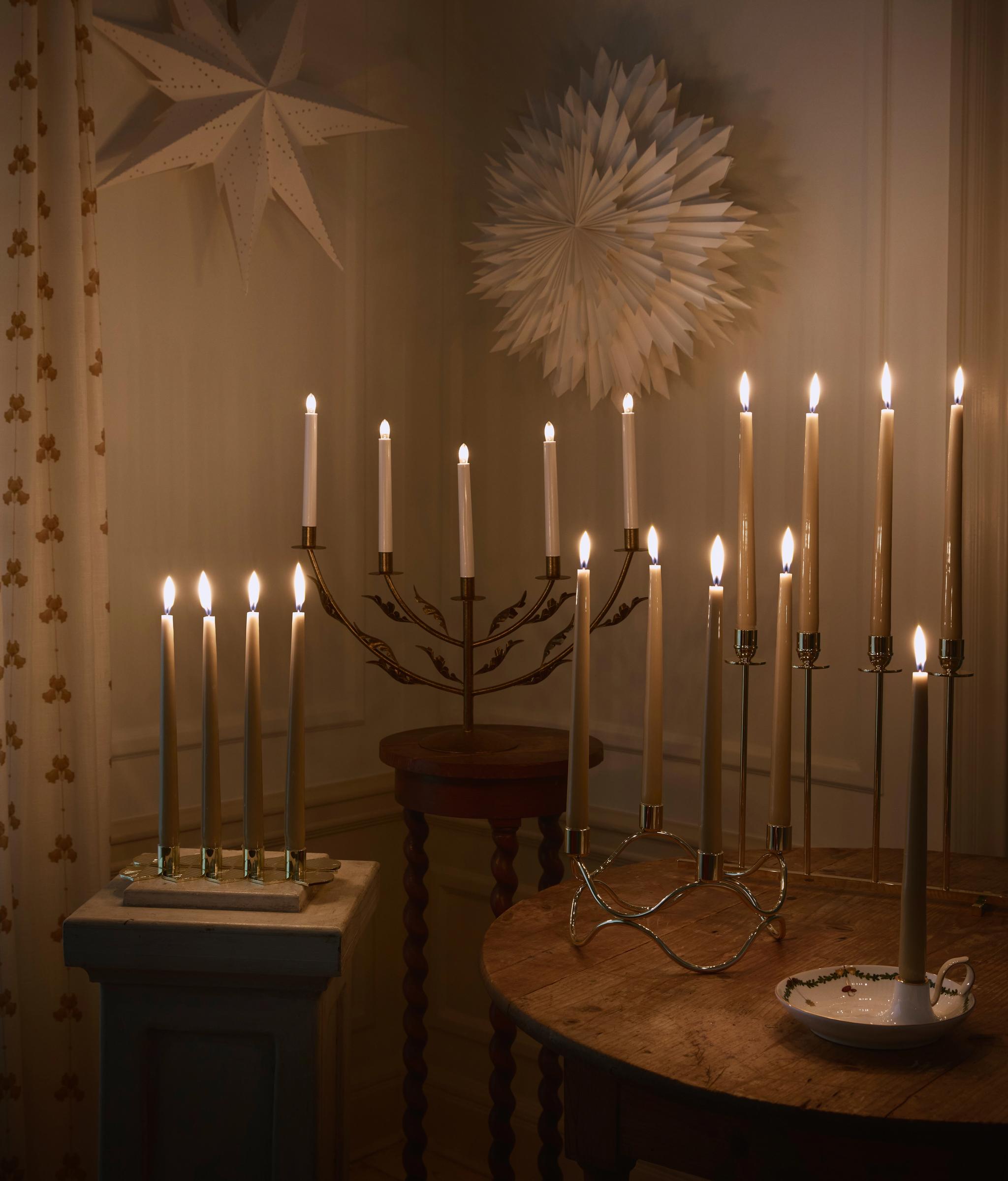 Julestjerner og tente adventsstaker mot en hvit vegg