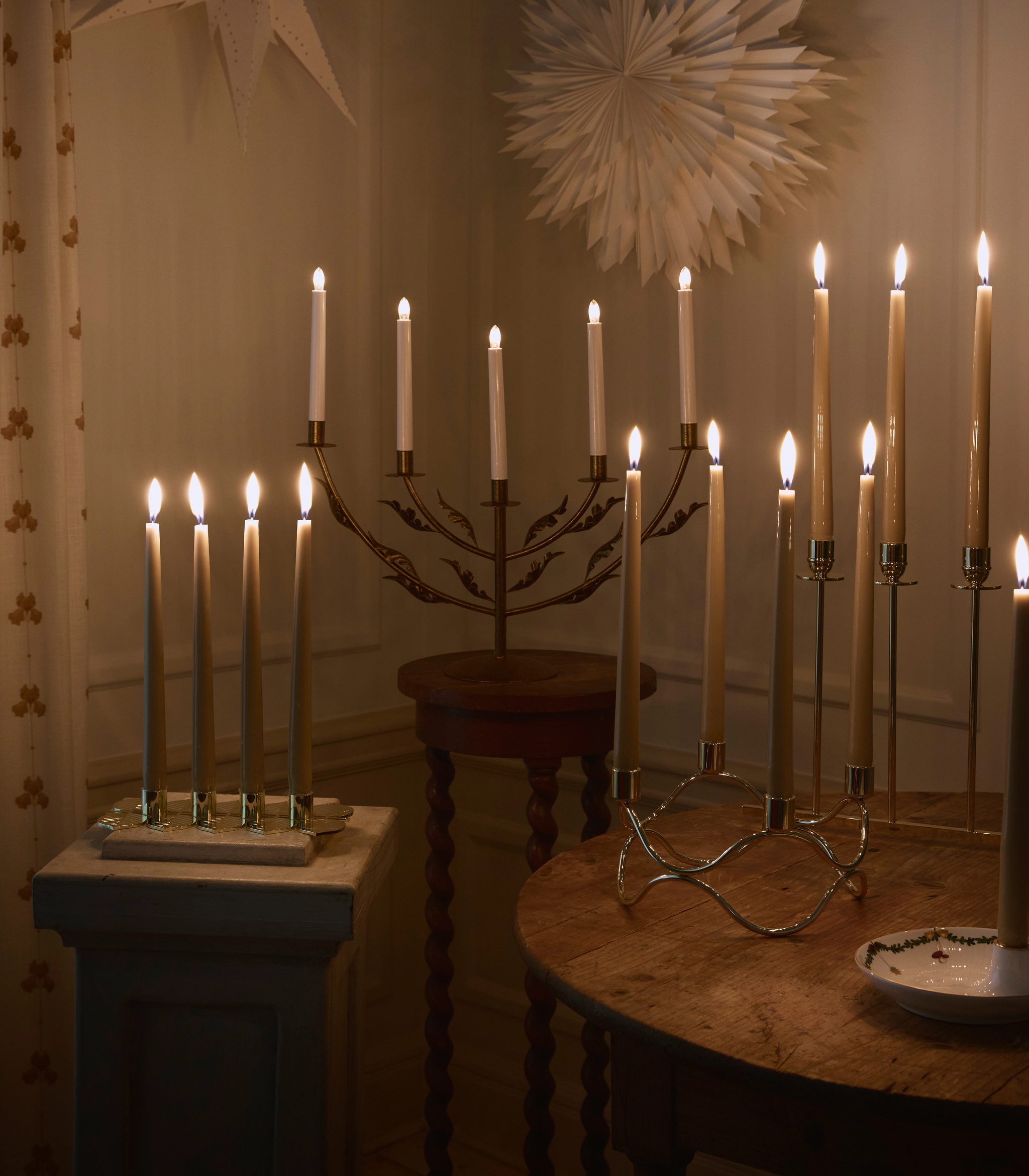 Julstjärnor och tända adventsljusstakar mot en vit vägg