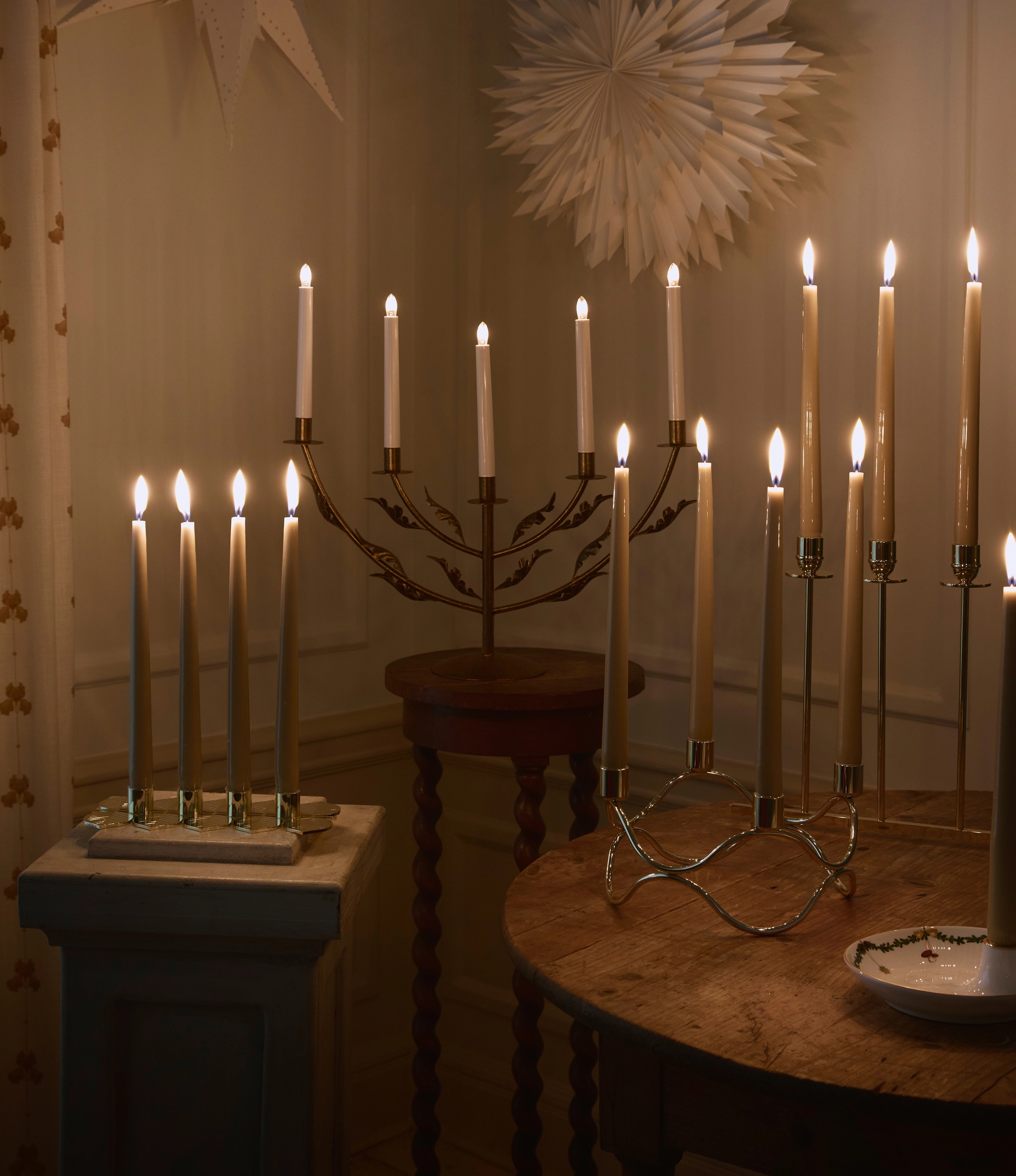 Julestjerner og tente adventsstaker mot en hvit vegg