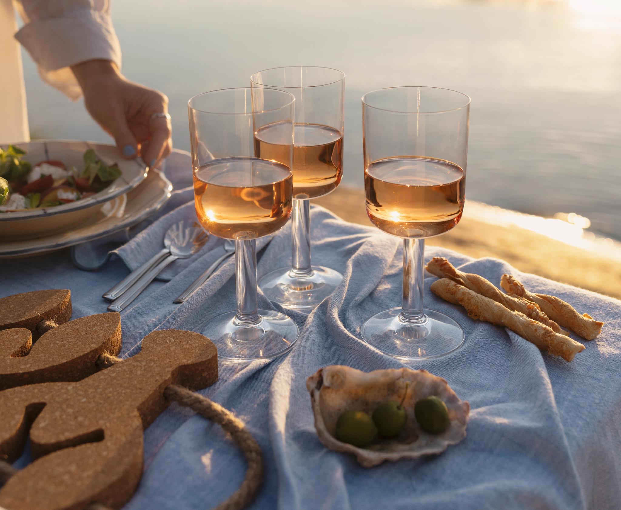 Somrig picknick med rosévin, snacks och sallad på dukat bord vid en stilla sjö i solnedgången.