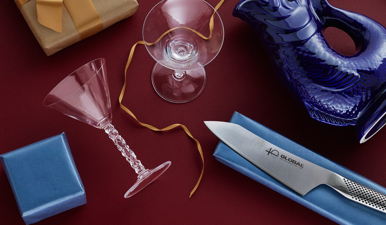 Blandade presenter inklusive en fiskformad kanna, kockkniv, glas och inslagna lådor mot röd bakgrund.