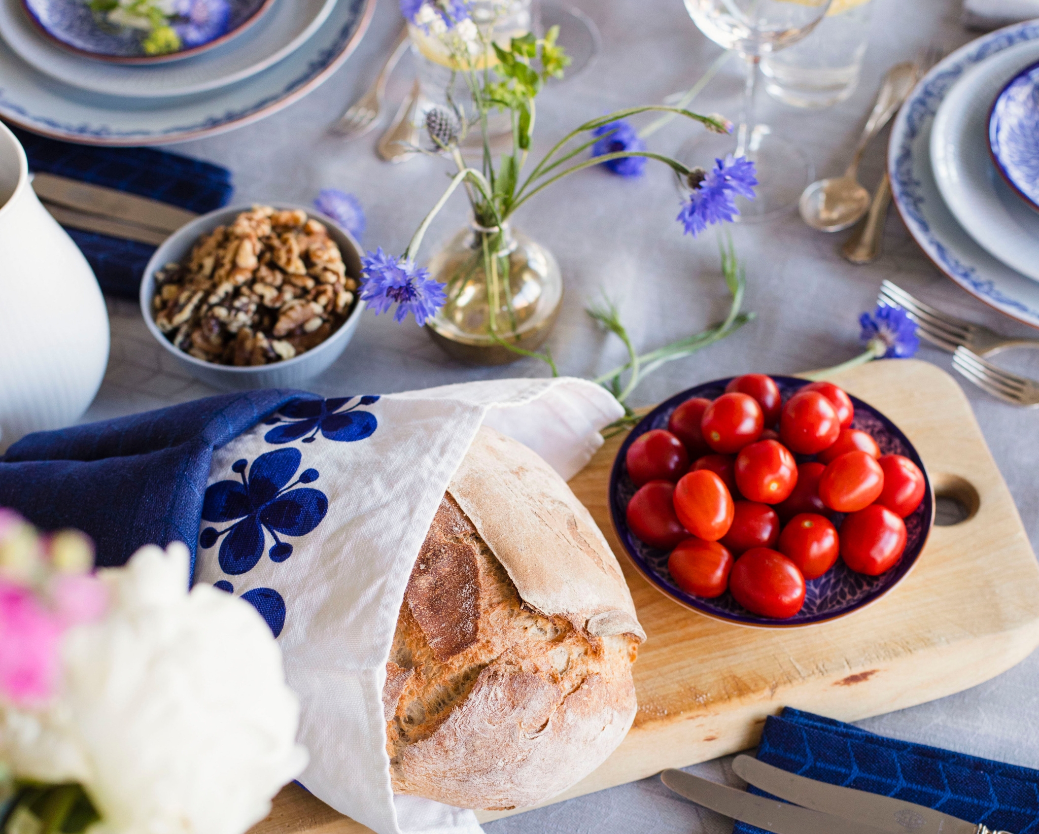 Bröd och tomater på en skärbräda på ett festligt dukat bord med ljusblå duk