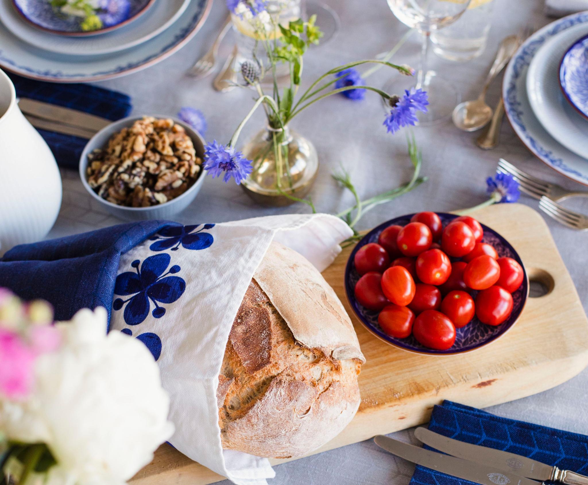 Bröd och tomater på en skärbräda på ett festligt dukat bord med ljusblå duk