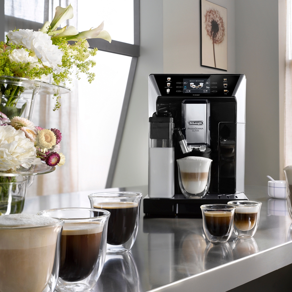 Latteglas på bänk vid en kaffemaskin med skummig latte i