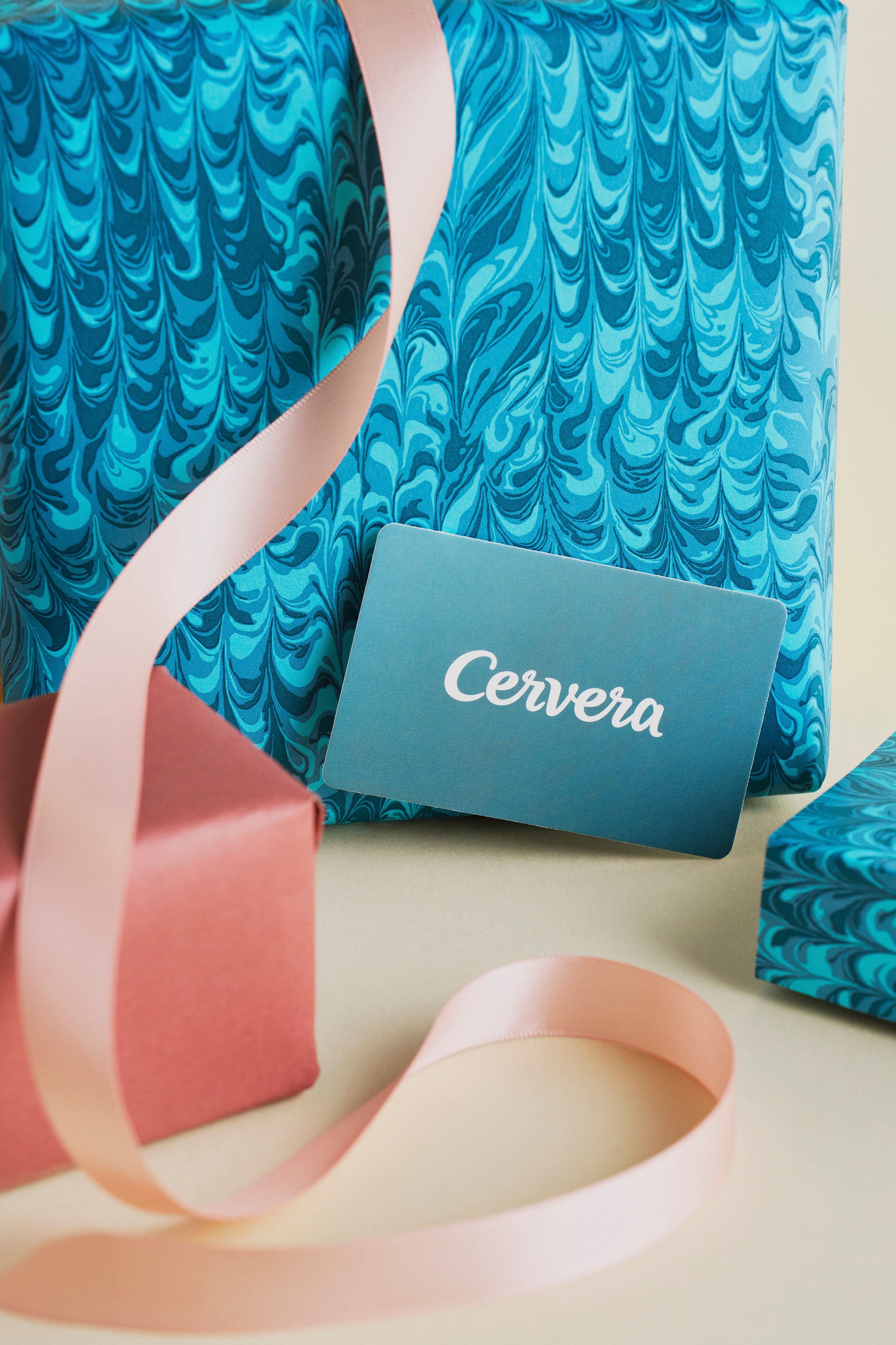 Ett Cervera-presentkort omgivet av presenter i blå marmorerat papper och en röd ask med ett rosa band