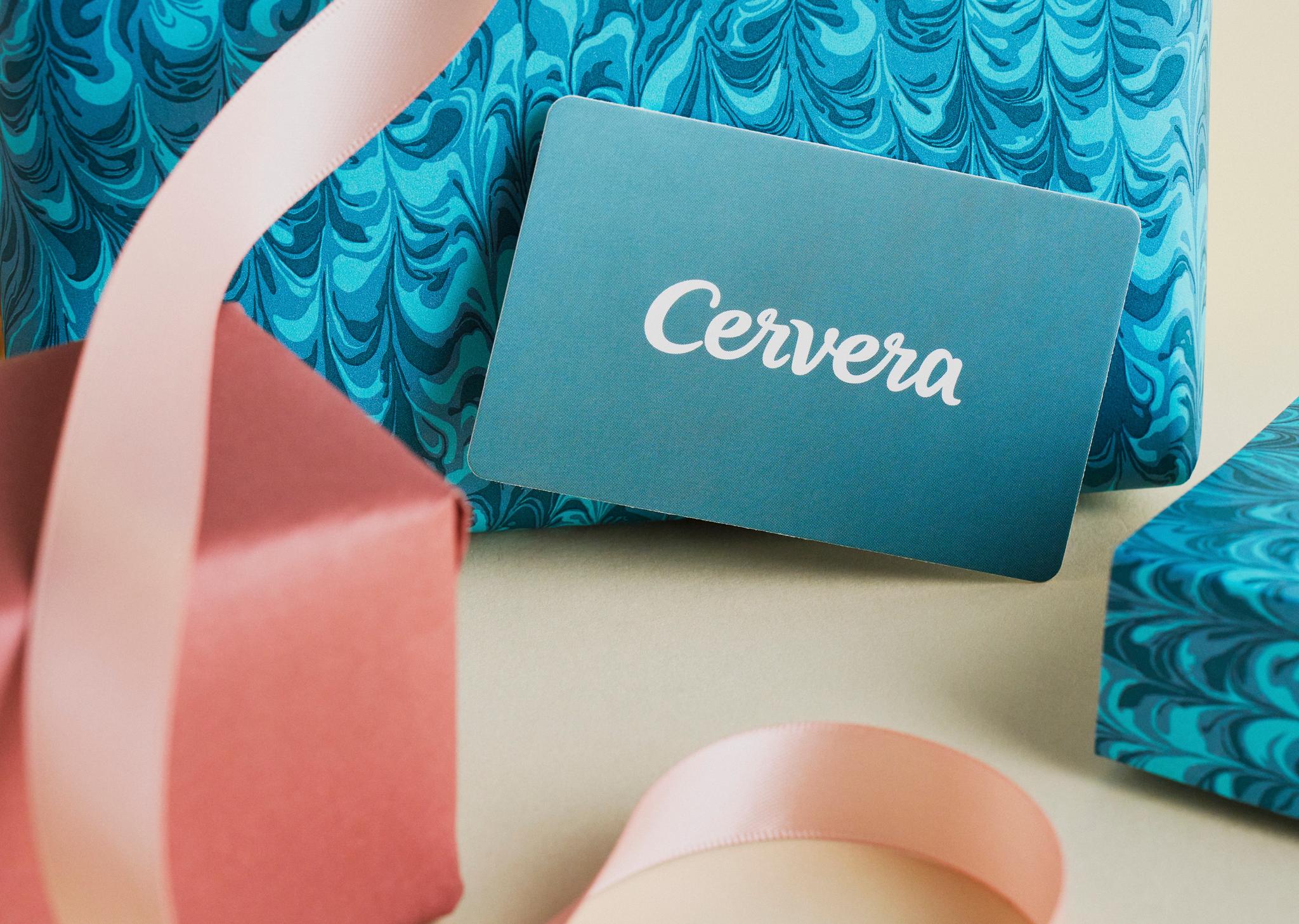 Ett Cervera-presentkort omgivet av presenter i blå marmorerat papper och en röd ask med ett rosa band