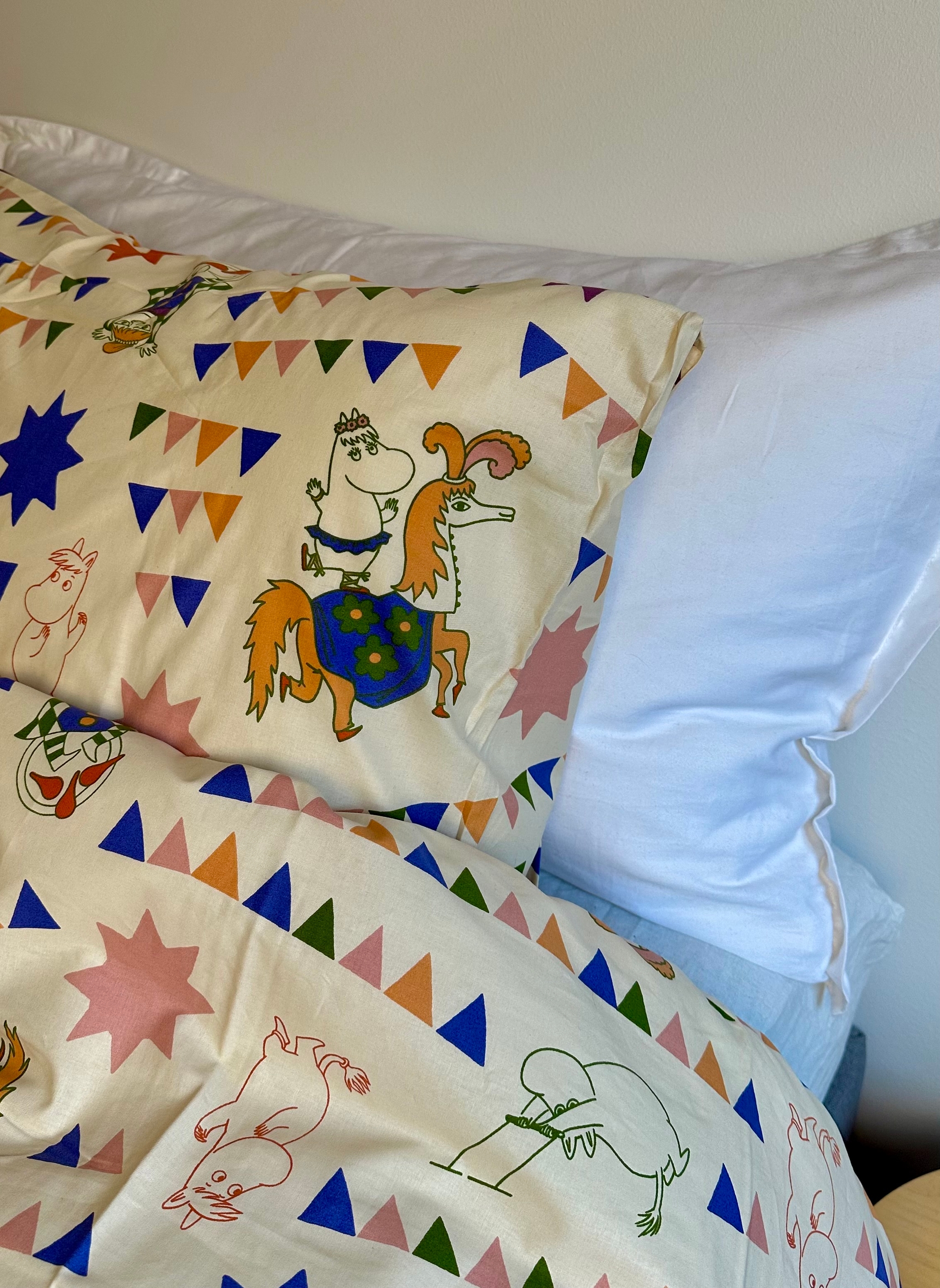 Moomin-themed duvet and pillow with colorful flags and characters, next to a plain white pillow.