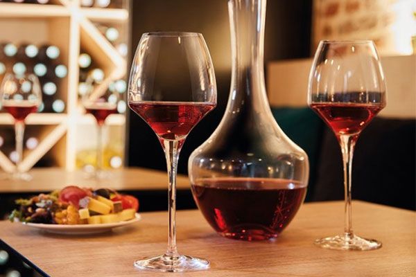 Två glas rött vin och en vinkaraff står på ett bord i en stämningsfull vinbar.