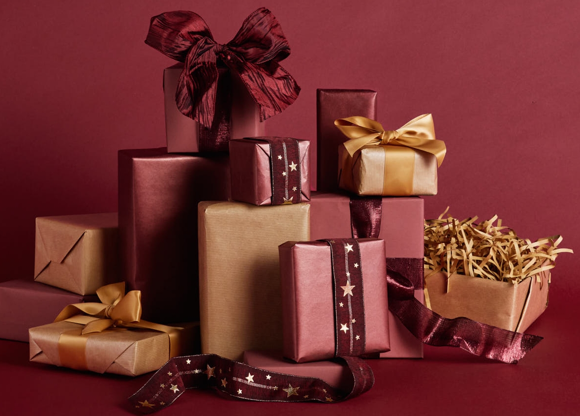 En hög med röda, rosa och guldinslagna presenter på en matchande röd bakgrund.