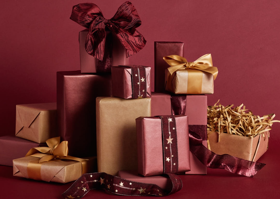 En hög med röda och guldfärgade inslagna presenter på en mörkröd bakgrund.