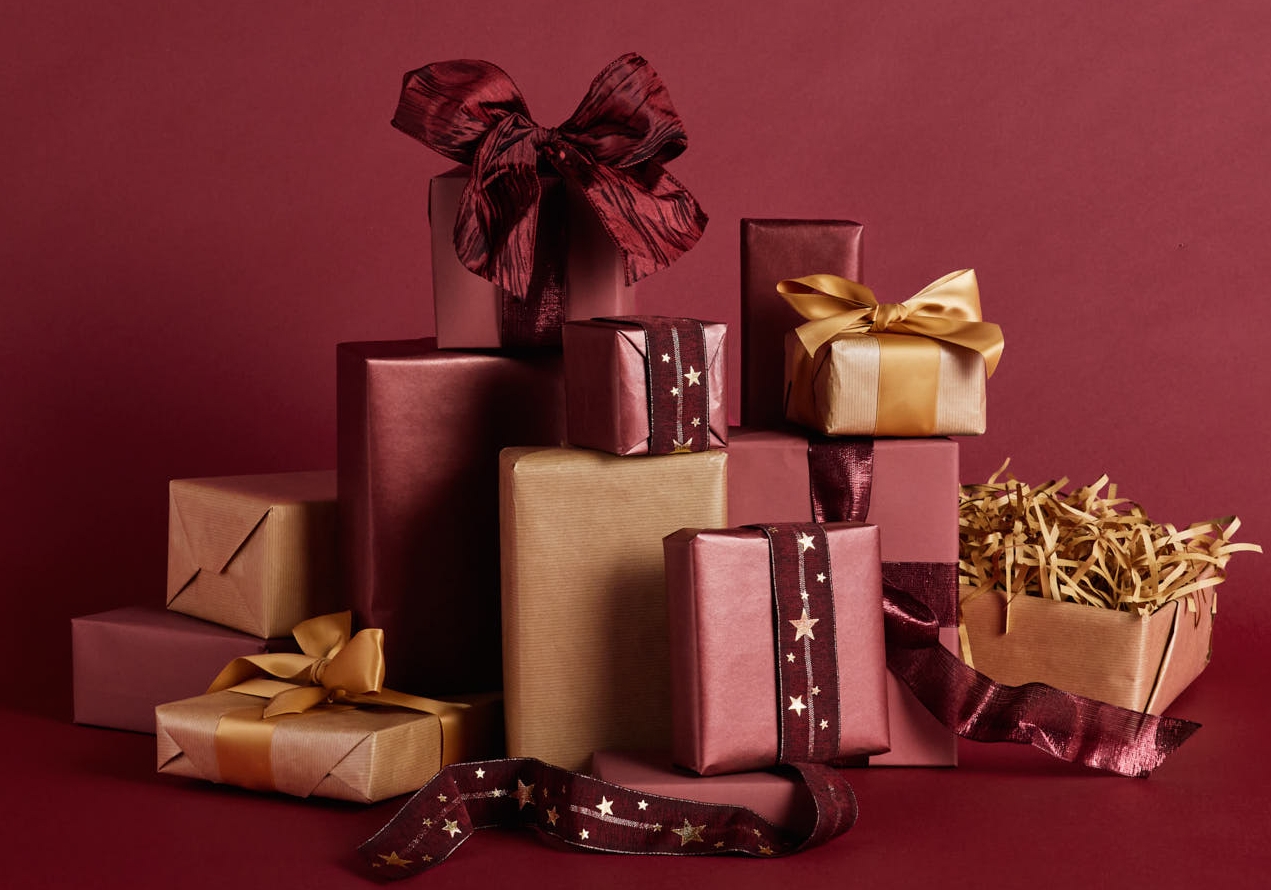 En hög med röda och guldfärgade inslagna presenter på en mörkröd bakgrund.