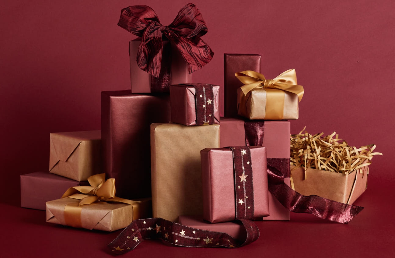 En hög med röda, rosa och guldinslagna presenter på en matchande röd bakgrund.