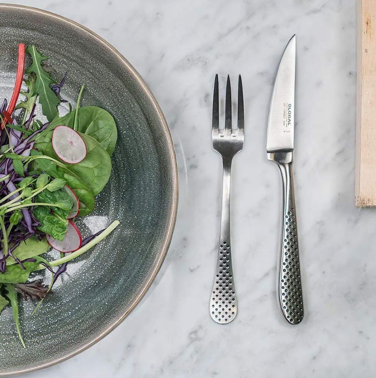 Global bestick på marmorbänk med en tallrik med grön sallad på