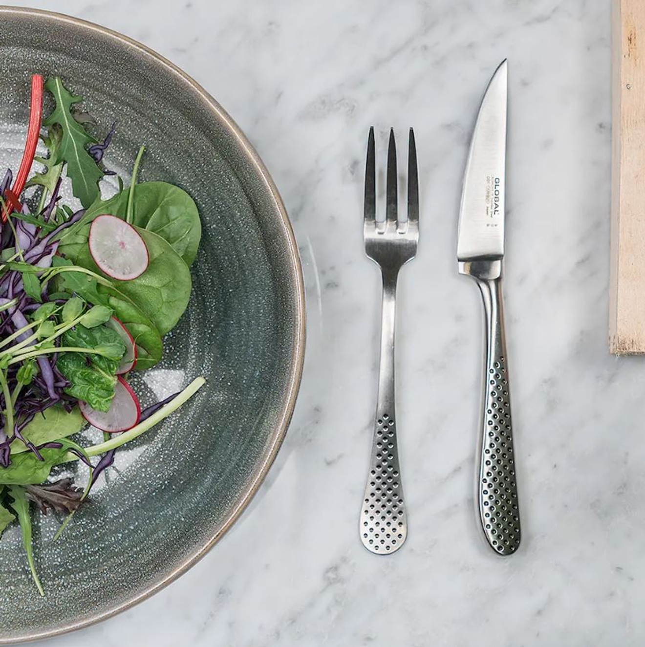 Global bestick på marmorbänk med en tallrik med grön sallad på