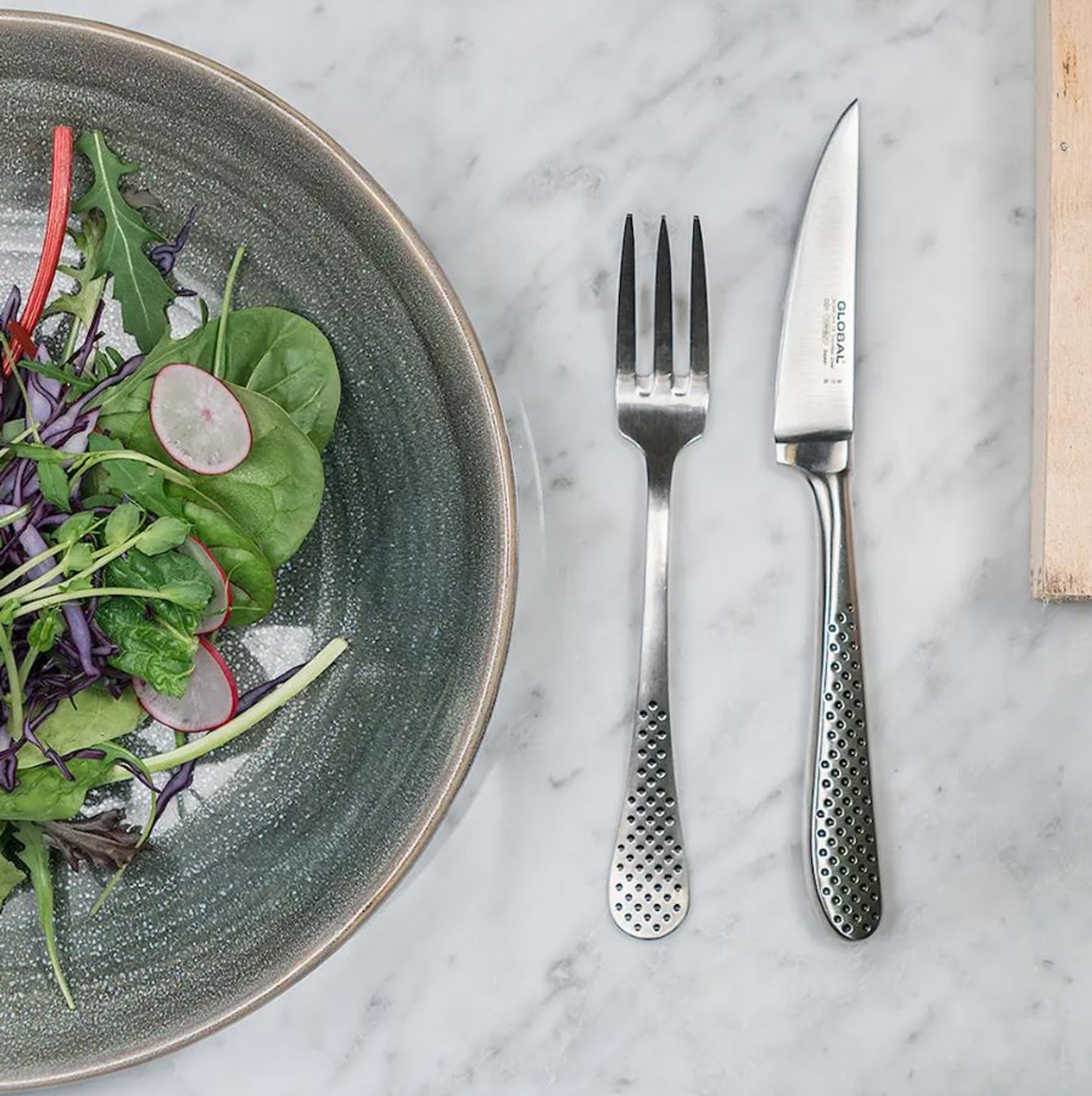 Global bestick på marmorbänk med en tallrik med grön sallad på