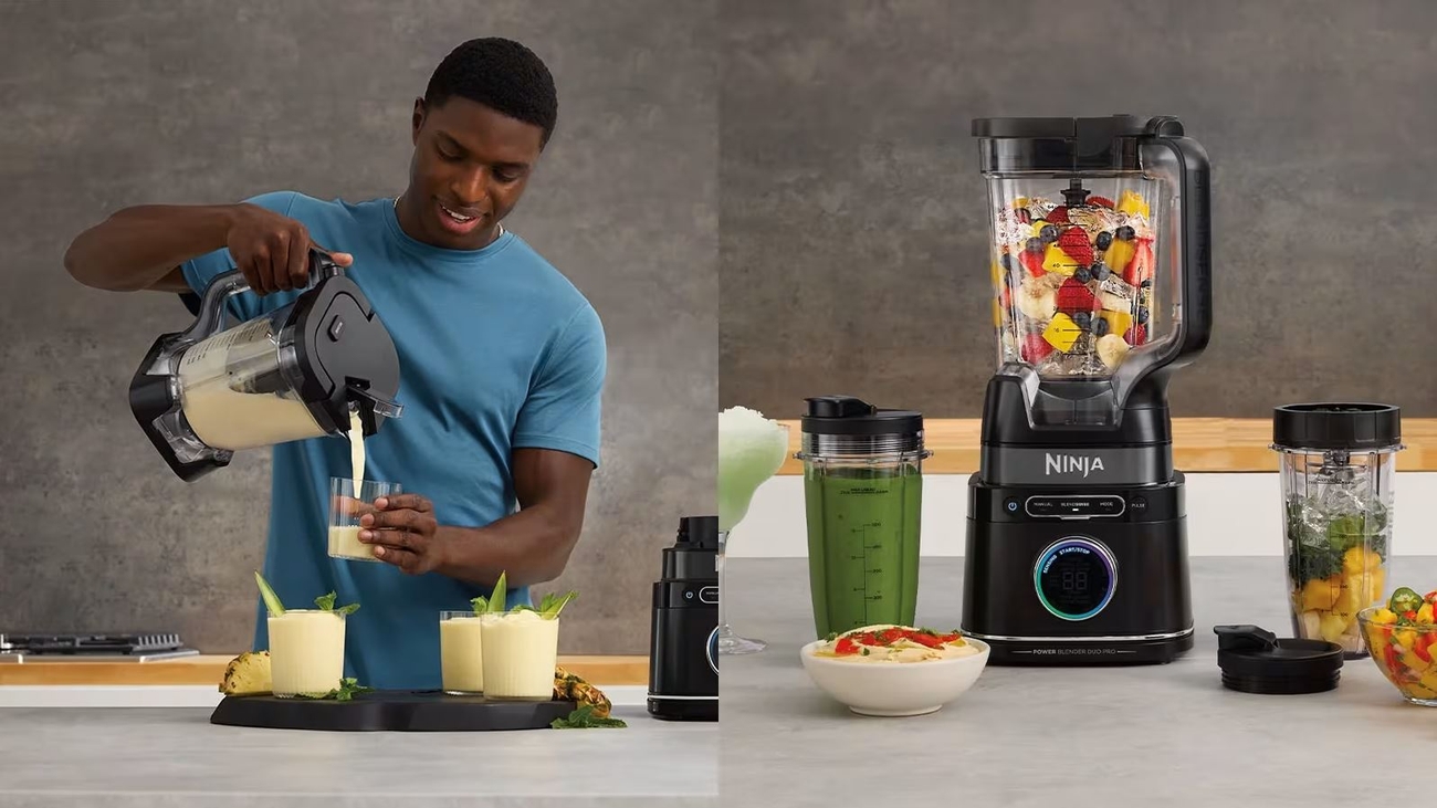 A man pours a smoothie from a Ninja blender into a glass, next to the blender with a pitcher of fruit, personal cups with smoothies, and chopped ingredients.