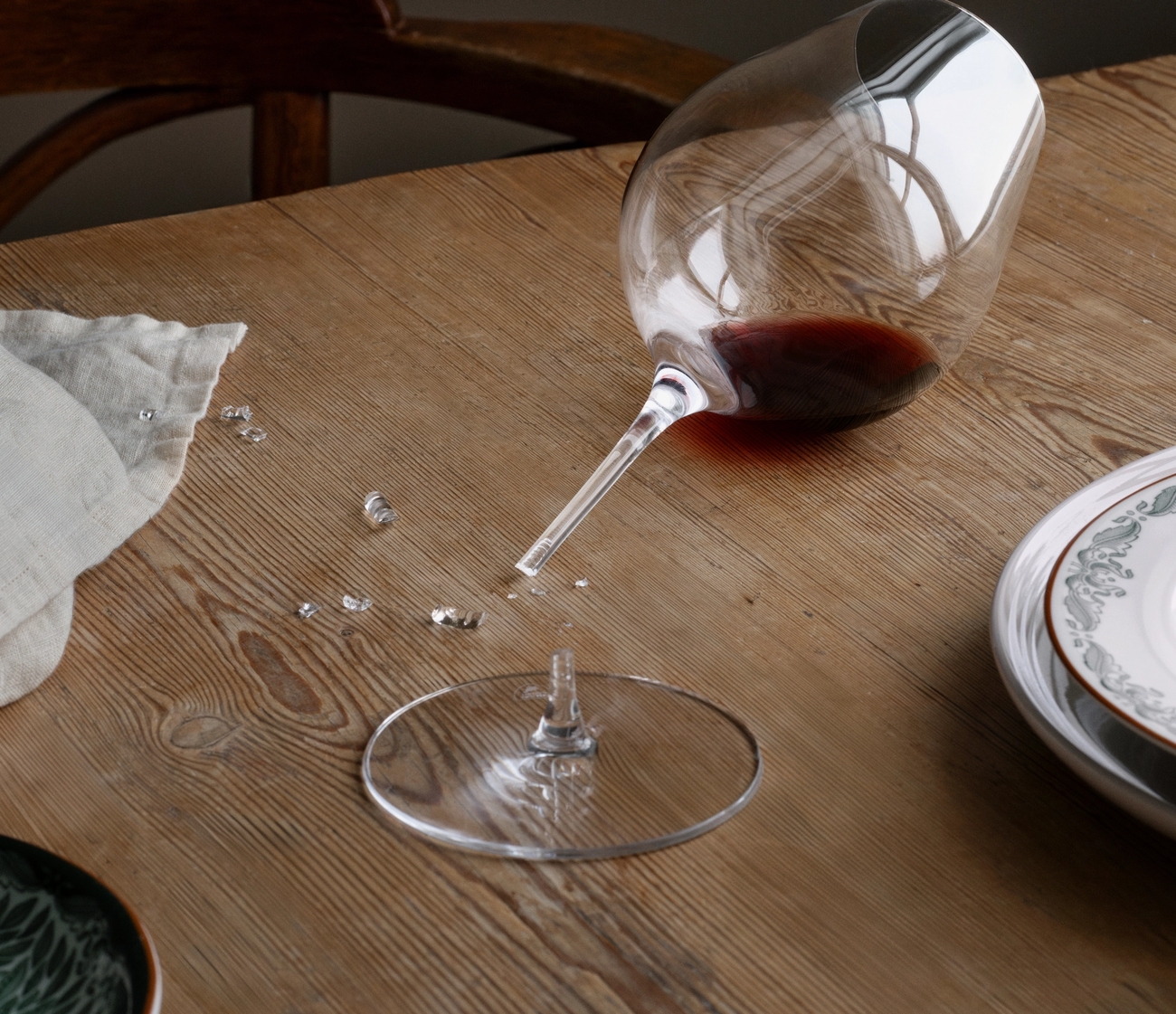 Ett trasigt vinglas med spillt rött vin och skärvor på ett träbord.