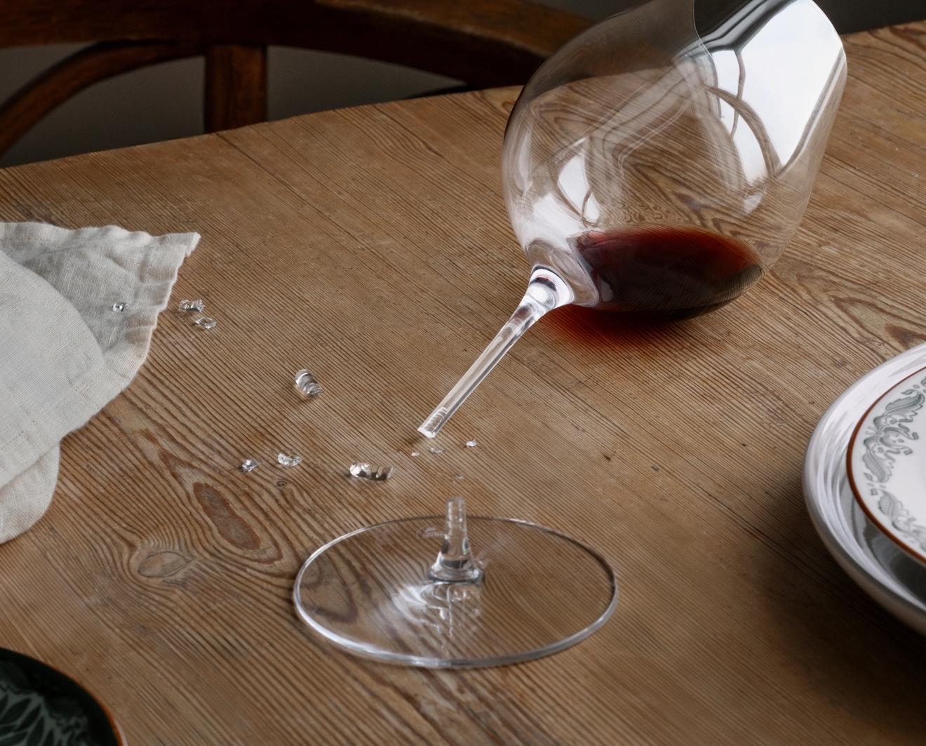 Ett trasigt vinglas med spillt rött vin och skärvor på ett träbord.