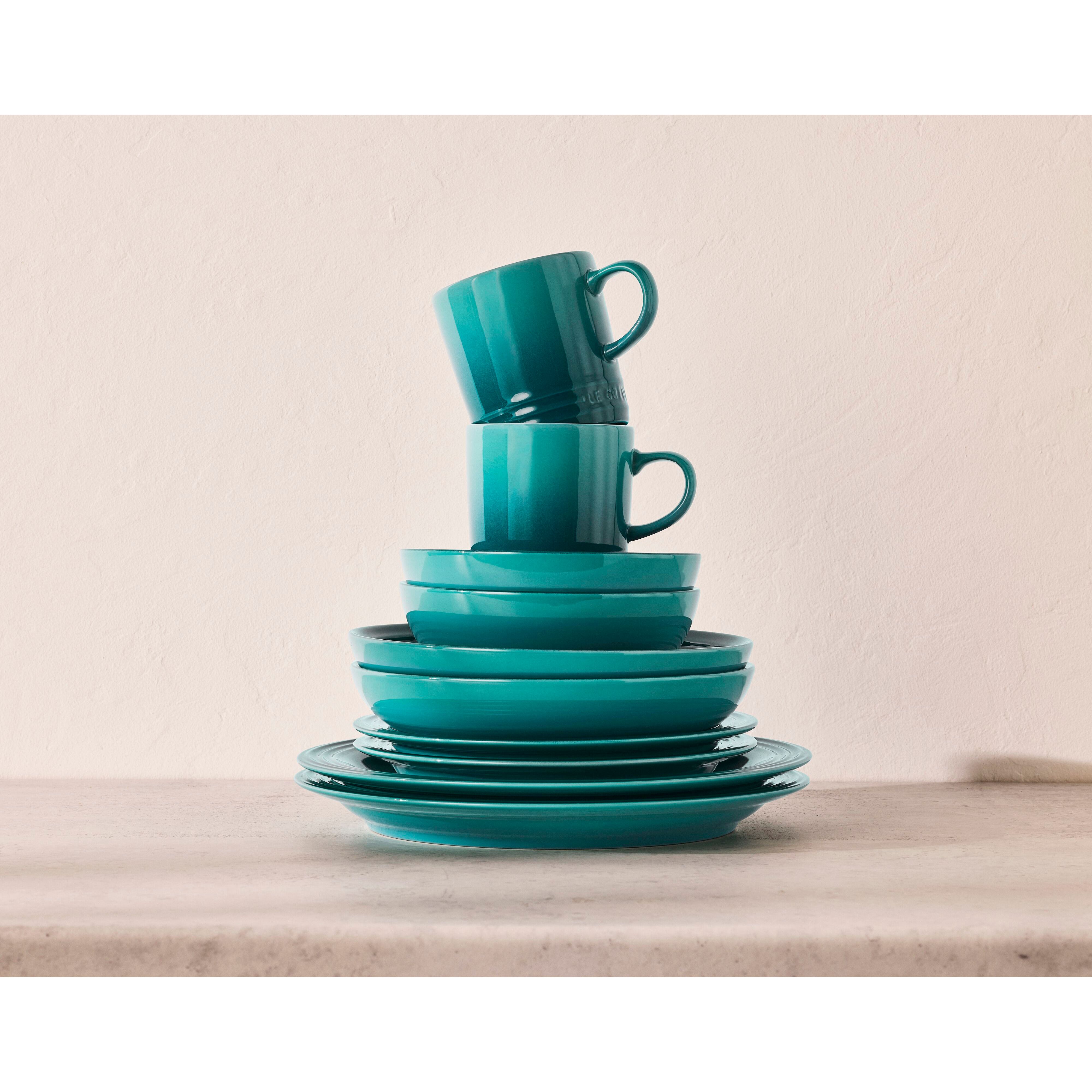 Grönblå tallrikar, skålar och muggar som är staplade på varandra.