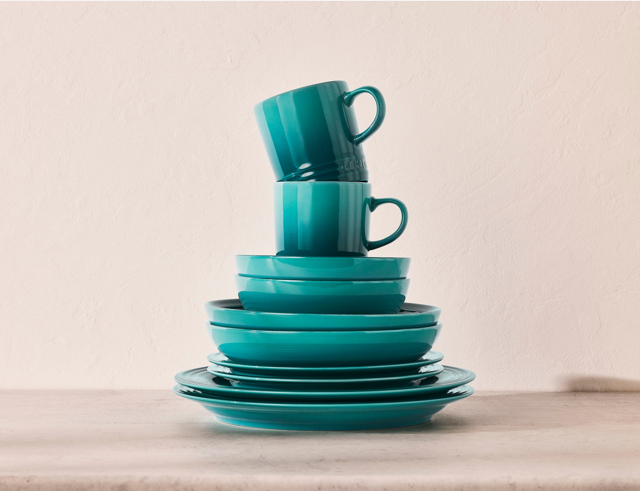 Grönblå tallrikar, skålar och muggar som är staplade på varandra.