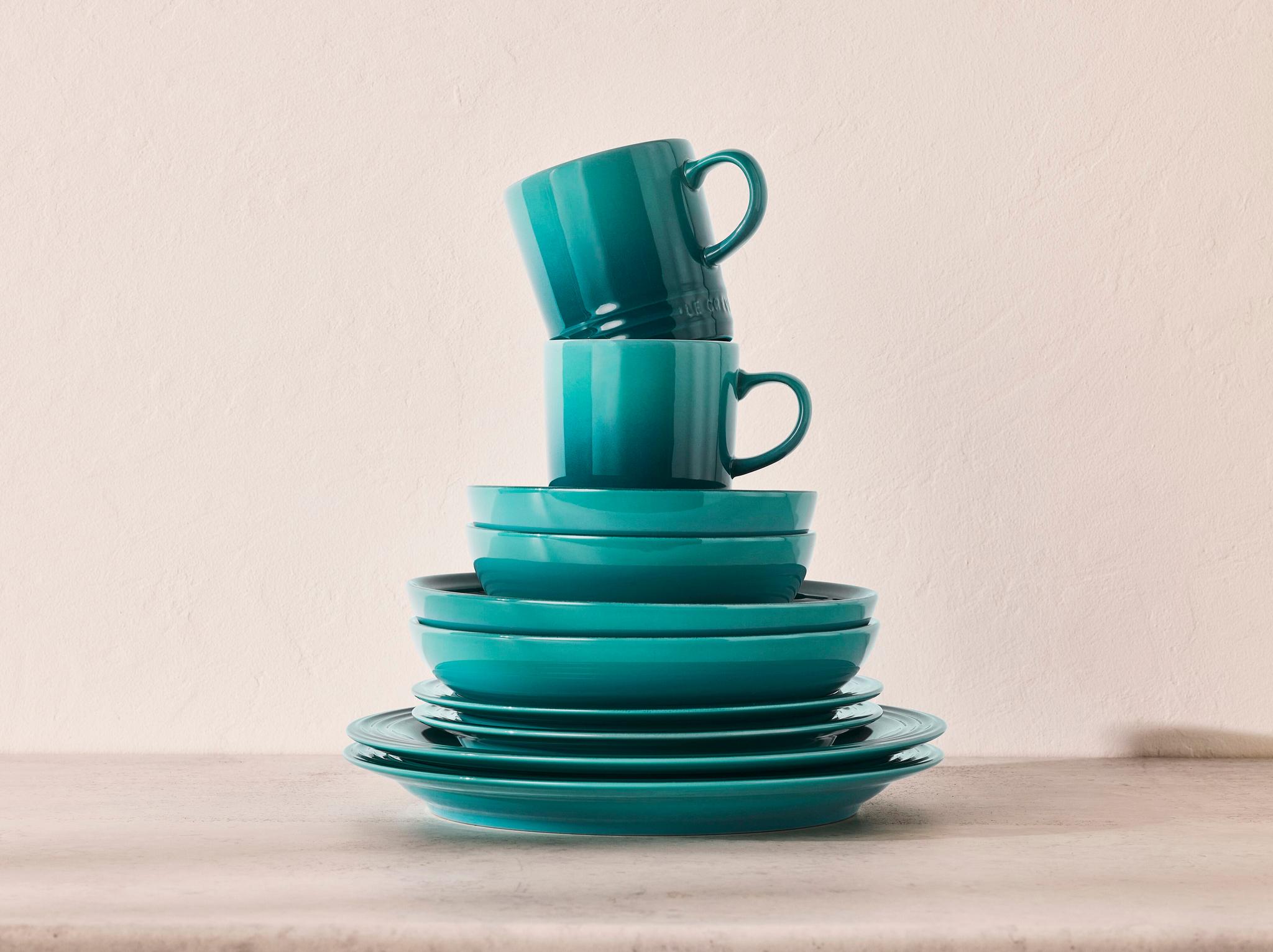 Grönblå tallrikar, skålar och muggar som är staplade på varandra.