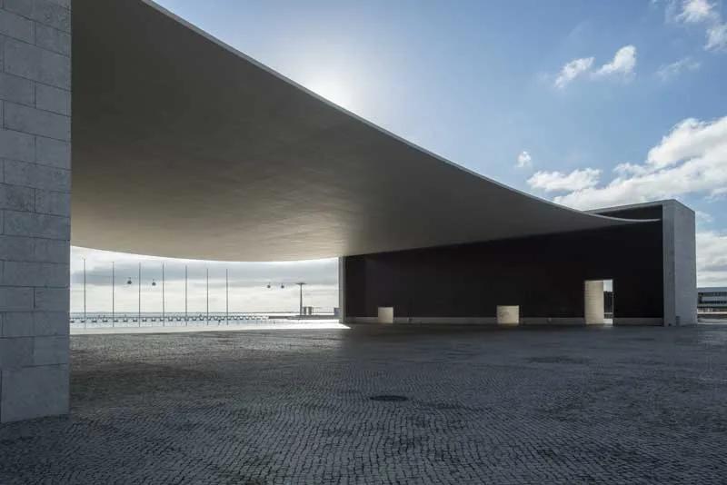 Pavilhão de Portugal Grande pala de concreto curva suspensa entre dois volumes, cobrindo uma praça