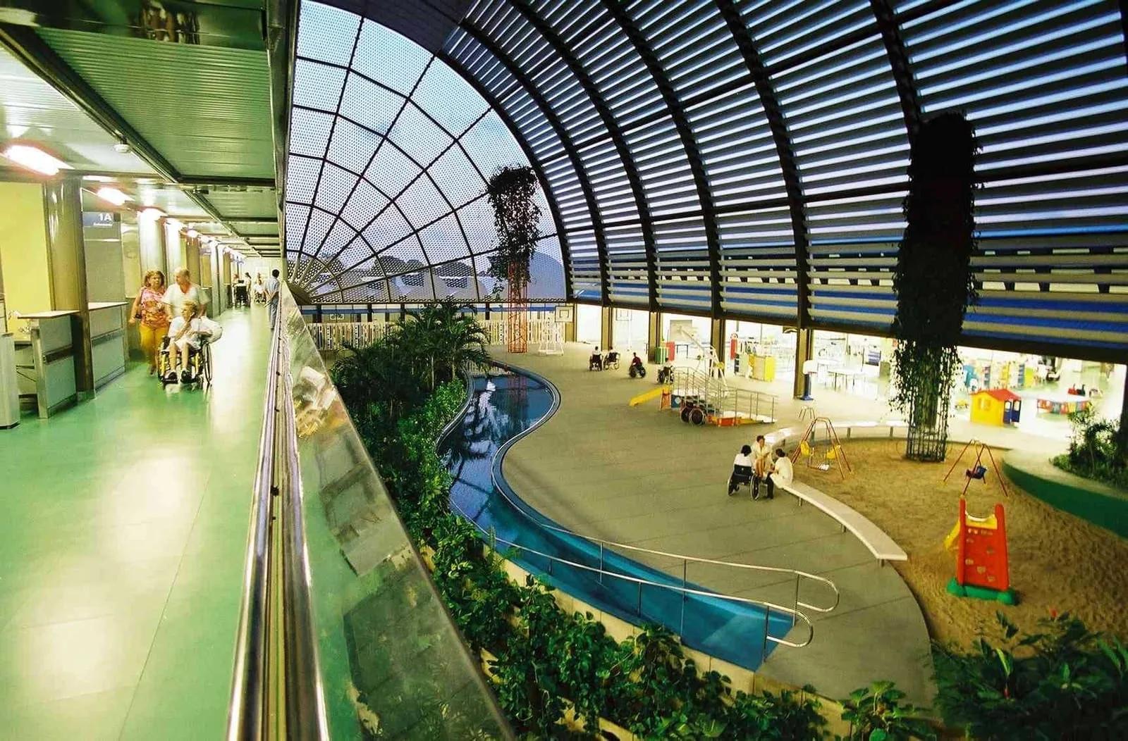 Interior do Hospital Sarah de Fortaleza, com cobertura curva de vidro, jardim, piscina e área de terapia