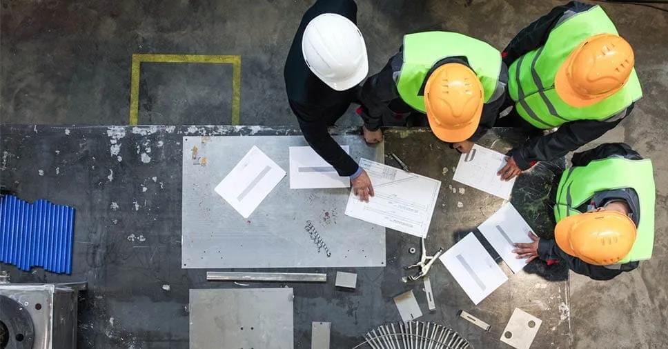 Equipe de obra reunida sobre os desenhos do projeto Vista de cima de engenheiros e arquitetos de capacete e colete discutindo desenhos sobre uma mesa no canteiro