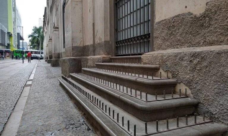 Pregos em degraus de edifício: arquitetura hostil no Brasil Degraus de pedra de um prédio antigo cobertos por fileiras de pregos metálicos voltados para cima, ao lado de uma calçada