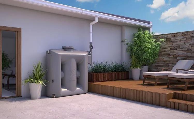 Cisterna para aproveitamento de água da chuva Cisterna cinza ligada à calha do telhado, ao lado de vasos de plantas e de um deck de madeira