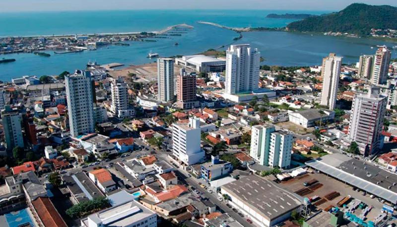 Centro de Itajaí e a foz do rio Itajaí-Açu Vista aérea do Centro de Itajaí, com prédios residenciais, o rio Itajaí-Açu, os molhes da barra e o mar ao fundo