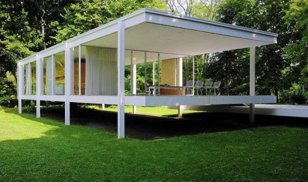 Casa Farnsworth, de Mies van der Rohe Casa de vidro elevada do chão por pilares brancos de aço, cercada por árvores e gramado