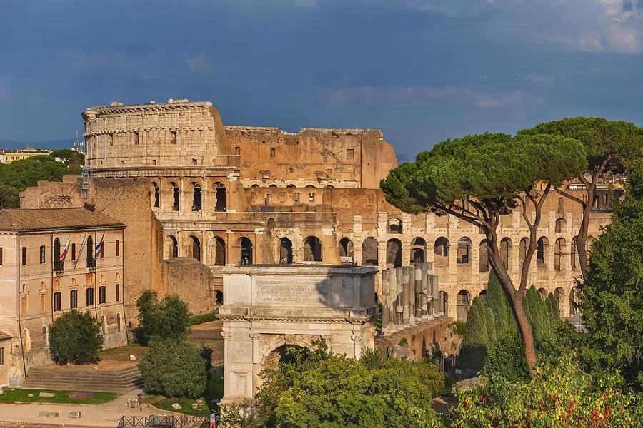 Arco de Tito e o Coliseu Vista de Roma com o Coliseu ao fundo e o Arco de Tito entre as árvores