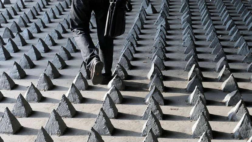 Chão coberto por fileiras de pequenas pirâmides de concreto, com uma pessoa caminhando entre elas