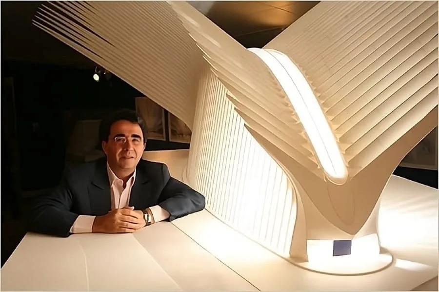 Santiago Calatrava sentado ao lado de uma grande maquete branca de estrutura em forma de asas