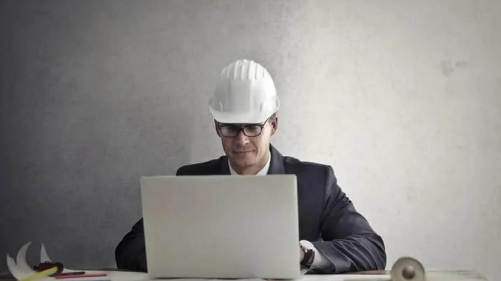 Engenheiro de capacete de obra branco mexendo no computador fazendo curso online.