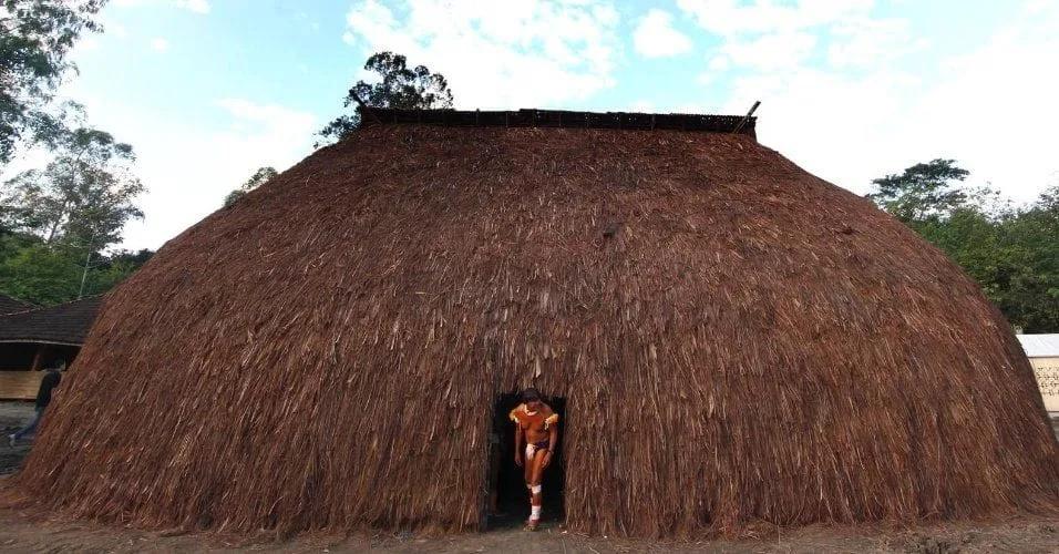 Grande casa indígena de palha em forma arredondada, com uma criança na porta