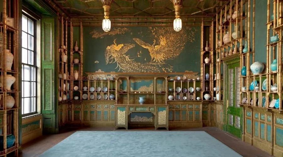 Peacock Room Sala com paredes de painéis de madeira e prateleiras douradas com porcelanas, e um grande painel de pavões na parede do fundo