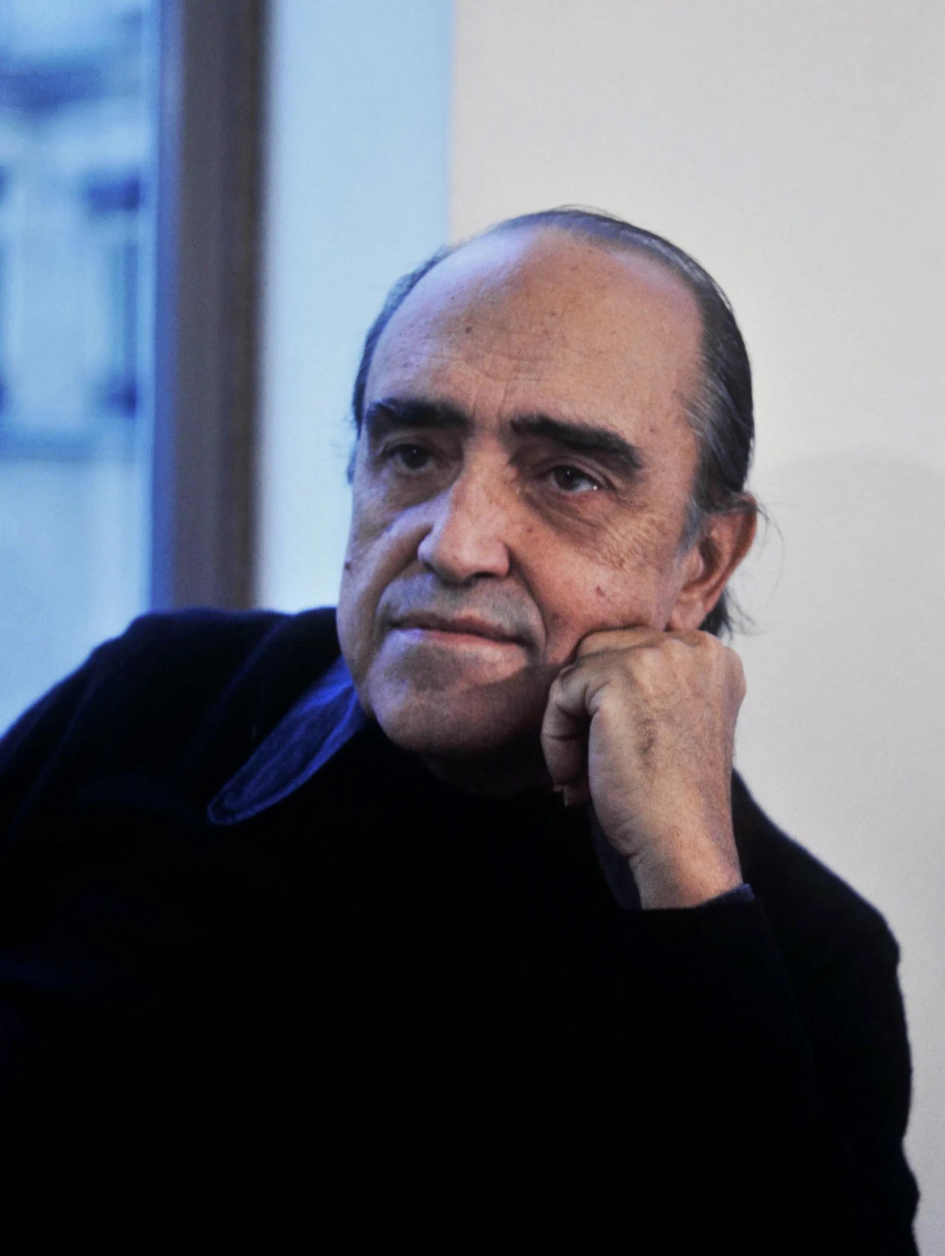 Retrato em preto e branco de Oscar Niemeyer sentado, com a mão apoiada no queixo.