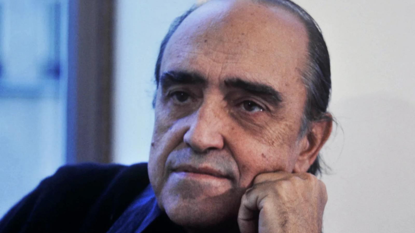 Retrato em preto e branco de Oscar Niemeyer sentado, com a mão apoiada no queixo.