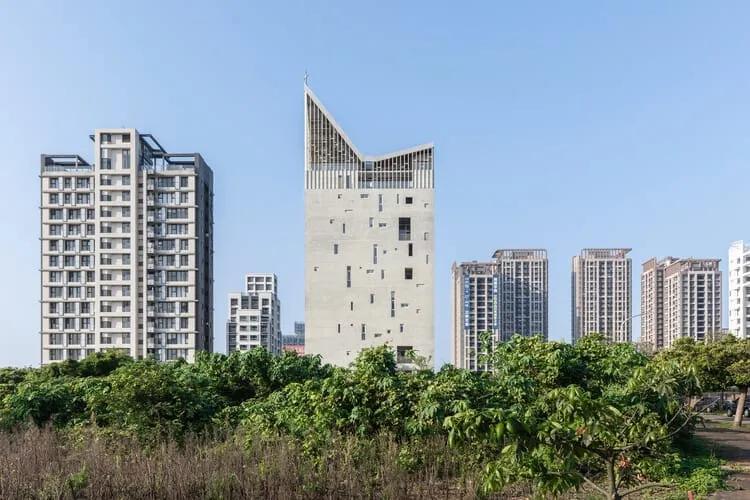 Torre de concreto com janelas em arranjo irregular e cobertura assimétrica que termina em ponta com uma cruz